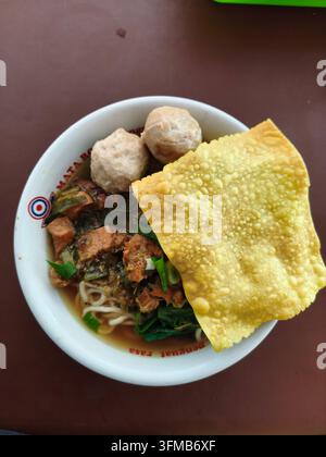 Schüssel mit Nudeln, grünen Blattgemüsen, Fleischbällchen, knusprigen Crackern und einer Scheibe Fisch in einer lebendigen kulinarischen Umgebung Stockfoto