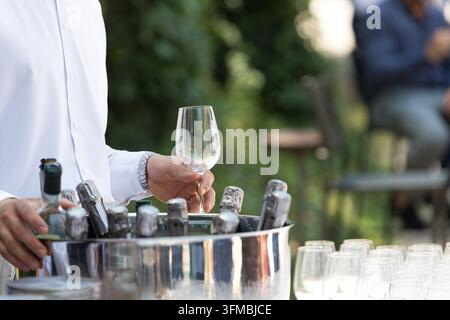 Kellner bereitet Weingläser und Champagnerflaschen in einem Eiskübel für eine Veranstaltung im Freien vor Stockfoto