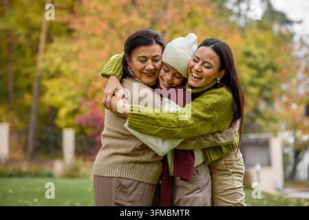 Mutter, Großmutter und Großtochter sitzen auf hölzerner Terrasse und umarmen sich. Stockfoto