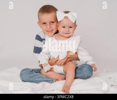 zwei entzückende Kinder, die sich herzlich in einem gemütlichen Indoor-Studio umarmen, umgeben von einer weichen Decke und einem plüschigen Stofftier, in einer Nahaufnahme des Auges aufgenommen Stockfoto