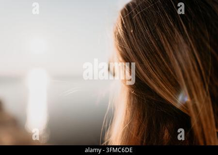 Haarwasser bei Sonnenuntergang Nahaufnahme einer Frau mit langen blonden Haaren, die die über einen ruhigen See untergehende Sonne betrachtet Stockfoto