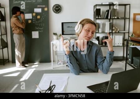 Frau hört Musik mit Kopfhörern und tanzt am Schreibtisch im Büro Stockfoto