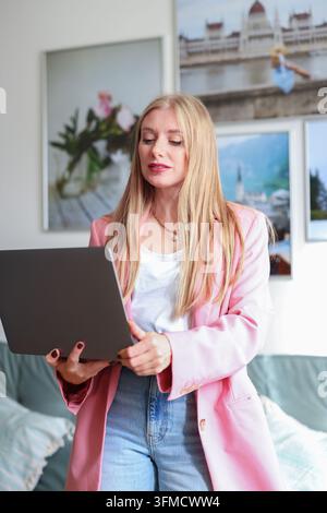 Junger Profi lächelt, während er einen Laptop trägt, perfekt für Kampagnen über Technologie, Führung und Karrierenerfolg. Stockfoto
