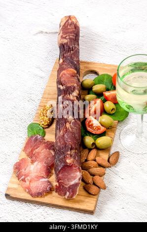 Ganze luftgetrocknete Wurst und geschnittenes Fleisch auf einem Holzbrett mit grünen Oliven, Kirschtomaten, Spinat und Mandeln serviert Stockfoto