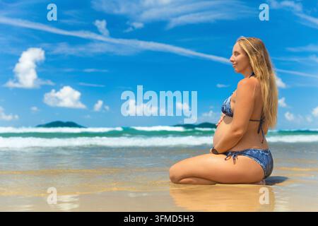 Neun Monate schwangere Frau im dritten Trimester meditiert und entspannt sich an einem tropischen Meeresstrand. Gesunder pränataler Lebensstil, Reisen im Sommer Stockfoto