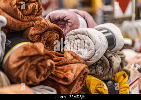 Gerollte Plüsch-Fleece-Decken in Braun, Rosa, Grau und Gelb werden in einem Haushaltswarenladen präsentiert. Stockfoto