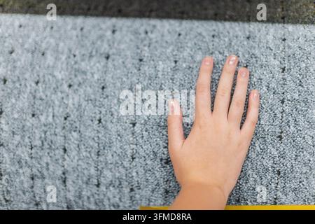 Eine Hand berührt die weiche, strukturierte Oberfläche eines grauen Teppichs. Stockfoto