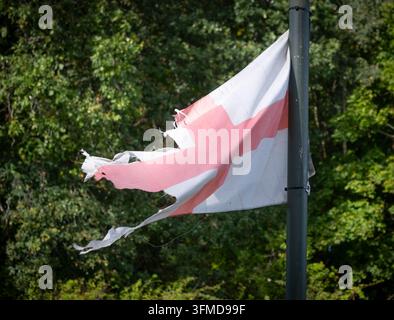 Zerrissene und zerfetzte Flagge von St. Georg weht immer noch im Wind, an einem Straßenlaternenpfosten befestigt, Worcestershire, England. Stockfoto