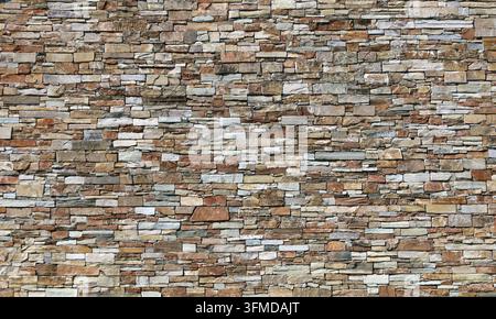Große Steinverkleidungswand aus gestapelten, gestreiften Ziegeln aus natürlichen mehrfarbigen Gesteinen. Hintergrund und Textur. Stockfoto