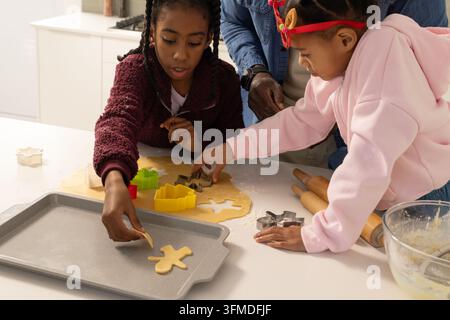 Afroamerikanische Familie mit zwei Kindern backt in der Küche und verwendet Ausstecher auf Weihnachtsplätzchenteig Stockfoto