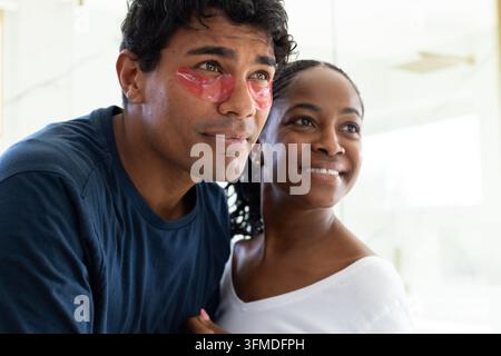 Afroamerikanisches Paar steht zu Hause, Mann trägt marineblaues Hemd und rosa Augenklappen. Porträt, Partner, Tageslicht, Innenraum, Fenster, minimalistisch, Leben Stockfoto