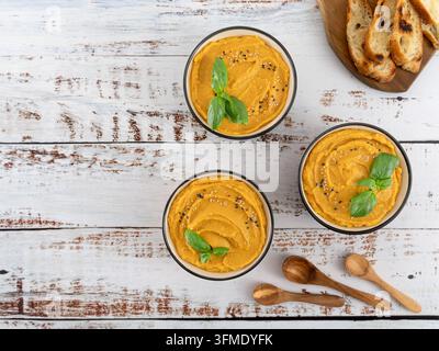Überkopf-Komposition von cremiger hausgemachter Kürbissuppe, serviert in Schüsseln mit frischem Basilikum auf einem rustikalen weißen Holztisch. Stockfoto