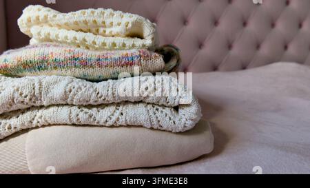 Nahaufnahme eines ordentlichen Stapels weicher gefalteter Strickpullover und eines beigen Sweatshirts auf einem rosa Bett. Stockfoto