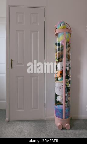 Moderner klarer zylindrischer Aufbewahrungsorganizer gefüllt mit bunten Stofftieren in einem Kinderzimmer. Stockfoto
