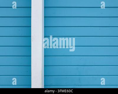 Horizontale blau lackierte Holzplanken zeigen subtile Holzmaserung und sanfte natürliche Beleuchtung. Ein weißer vertikaler Holzrahmenpfosten fügt geometrischen Kontrast hinzu Stockfoto