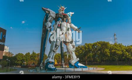 Ansicht der Freedom-Gundam-Statue, die vor dem Lalaport-Einkaufszentrum steht, umgeben von üppigen grünen Bäumen unter einem klaren blauen Himmel in Shanghai Stockfoto