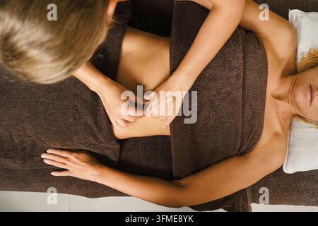 Oberansicht einer mittelalten Frau, die auf einer Massageliege im Spa liegt. Therapeut massiert ihren Bauch Stockfoto