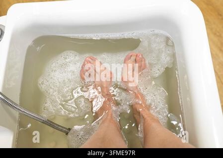 Fußbad-Konzept, ältere Frau macht ein hygienisches Fußbad in Wasser für weiche Fußhaut in einem Schönheitssalon, Spa-Pediküre, Fußtherapie mit einer entspannenden Stockfoto