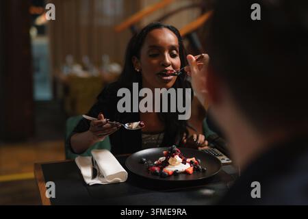 Paar hat Spaß, während es im Restaurant Dessert genießt, ein junger Mann füttert seiner begeisterten Freundin einen Bissen. Stockfoto