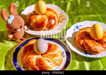 Drei Osterkränze mit farbigen Ostereiern auf bunten Tellern auf grüner, gekräuselter Tischdecke und Amigurumi-Osterhase Stockfoto