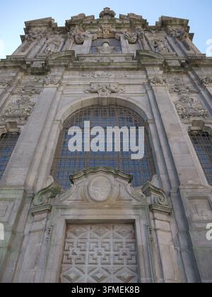 Ansicht der kunstvollen Steinfassade der Kirche São Ildefonso mit aufwendigen Schnitzereien, einem großen Rundbogenfenster und einer prächtigen Holztür in Porto Stockfoto