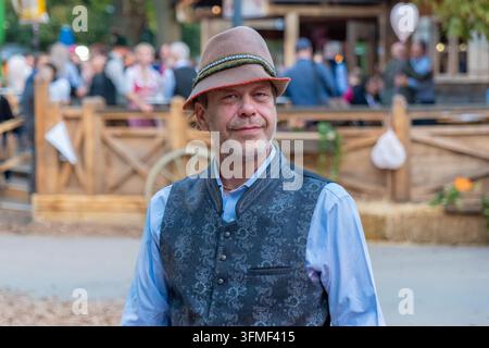 Ein lächelnder Mann in traditioneller bayerischer Tracht steht im Freien bei einer Oktoberfest-Feier. Stockfoto