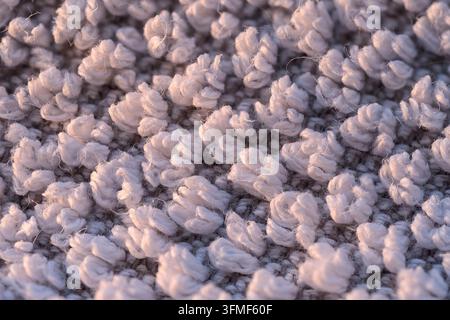 Nahaufnahme von weichem weißem Textil mit flauschigen geschlungenen Fasern und geringer Schärfentiefe, das abstrakte Textur, gemütliche Oberflächendetails und warmes Licht erzeugt Stockfoto