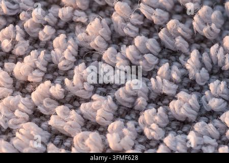 Nahaufnahme von flauschigen weißen Fasern auf dunkler gewebter Oberfläche, die einen weichen abstrakten Hintergrund mit sanften warmen Highlights und reichen Details bilden. Stockfoto
