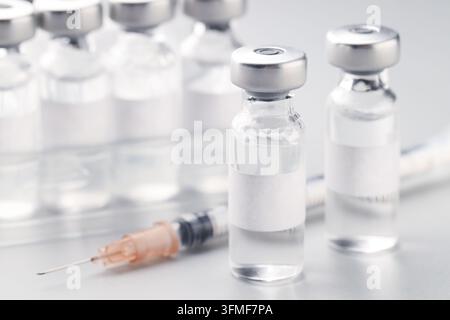 Fläschchen mit Impfstoff und Spritze auf weißem Tisch, Nahaufnahme Stockfoto