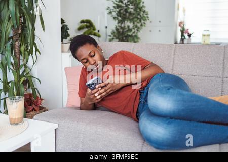 Junge Frau, die sich auf dem Sofa mit ihrem Smartphone entspannt Stockfoto