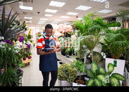Die junge Floristin macht Notizen auf ihrem Tablet und überprüft Blumen in einem Blumenladen Stockfoto