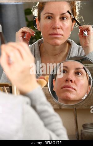 Mittlere blonde Frau mit lockigem Haar, die sich vor einem Spiegel schminkt Stockfoto
