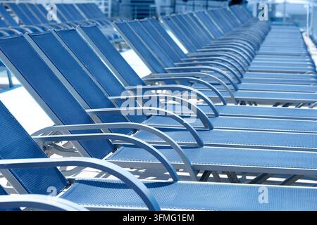 Lange Reihe leerer blauer Liegestühle, die auf dem offenen Deck eines Kreuzfahrtschiffes angeordnet sind, bereit dafür, dass Passagiere sich in der Sonne entspannen können Stockfoto