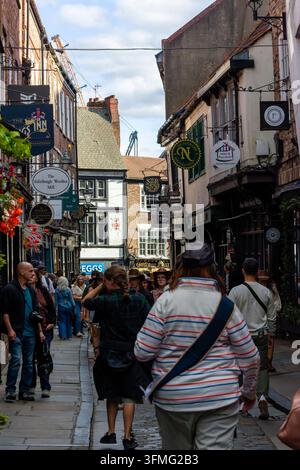 Fußgänger gehen die The Shambles in York, England, hinunter, Fachwerkgebäude aus dem Mittelalter und überhängende Ladenschilder säumen die schmale gepflasterte Gasse Stockfoto