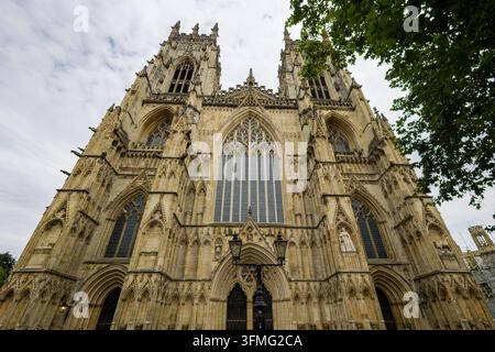 Gotische Westfassade der Kathedrale York Minster in Yorkshire, England, detaillierte Kalksteinfassade, die zu zwei Glockentürmen unter einem bewölkten Himmel aufragt Stockfoto