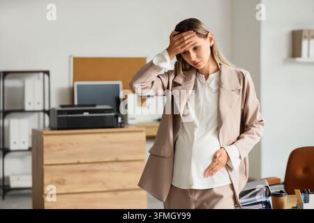 Burnout und Schwangerschaftsstress, müde schwangere Geschäftsfrau mit Kopfschmerzen und Erschöpfung bei der Arbeit in einer modernen Büroumgebung Stockfoto