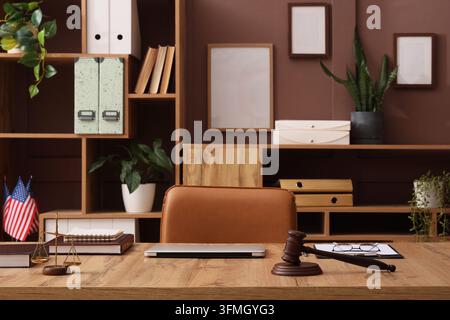 Büro einer Rechtsanwaltskanzlei mit Holzschreibtisch, Richterhammer und Waage der Gerechtigkeit in einem professionellen Arbeitsbereich mit amerikanischen Flaggen Stockfoto