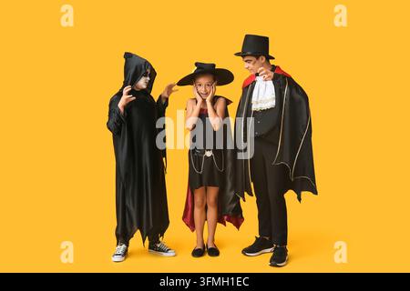 Halloween-Feier und kindliche Vorstellungskraft, vielfältige Kinder in gruseligen Kostümen, die zusammen mit Begeisterung auf einem leuchtend gelben Hintergrund spielen Stockfoto