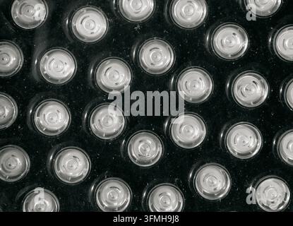 Nahaufnahme von wiederholten kreisförmigen silbernen LED-Leuchten, die über ein dunkles strukturiertes Panel angeordnet sind und ein reflektierendes High-Tech-Abstraktmuster erzeugen Stockfoto
