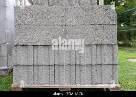 Ein Stapel grauer Betonblöcke, ordentlich auf einer Holzpalette auf einer Baustelle angeordnet. Diese haltbaren Mauerwerksmaterialien sind bereit für den Mauerbau Stockfoto