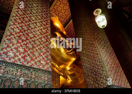 Nahaufnahme des Gesichts der goldenen liegenden Buddha-Statue, eingerahmt zwischen farbenfrohen Mosaiksäulen im Wat Pho Tempel in Bangkok Stockfoto