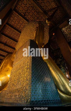 Nahaufnahme des Gesichts der goldenen liegenden Buddha-Statue, eingerahmt zwischen farbenfrohen Mosaiksäulen im Wat Pho Tempel in Bangkok Stockfoto