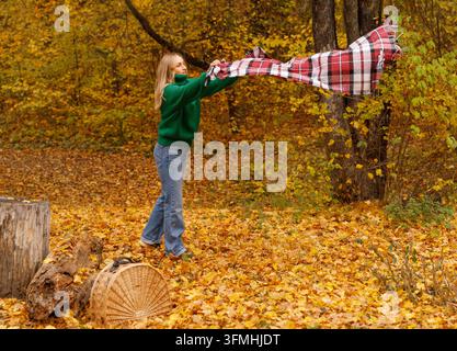 Frau breitet karierte Decke für Picknick im Herbstpark aus Stockfoto