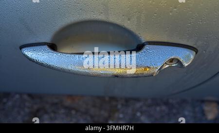 Autotürgriff, der mit Frost bedeckt ist. Morgendliche Kälte auf der Metalloberfläche sichtbar. Frostkristalle glitzern im weichen Licht. Perfekt für Winter- oder Reise-Themen Stockfoto