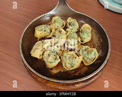Gebratene Knödel mit schwarzem Sesamsamen und gehackten Frühlingszwiebeln, serviert in einer warmen Gusseisenpfanne Stockfoto