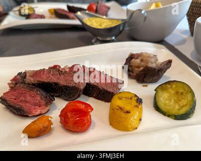 In Scheiben geschnittenes medium rare gegrilltes Steak mit Gemüse auf einem Teller. In Scheiben geschnittenes medium rare gegrilltes Steak auf einem weißen Teller serviert mit geröstetem Gemüse, Kirsch Stockfoto