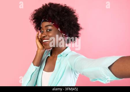 Buschige Afroamerikanische Dame, Die Selfie Macht, Posiert Sich Berührendes Gesicht Und Lächelt Vor Der Kamera Stehend Über Rosa Hintergrund, Studio-Aufnahme. Kopfaufnahme Von Pretty An Stockfoto