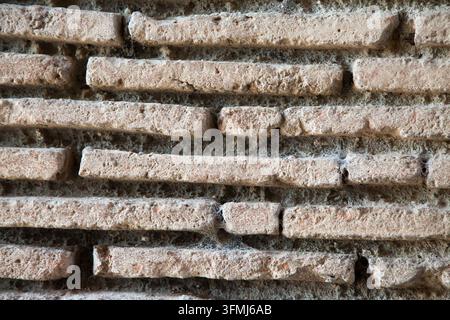 Verwitterte Ziegelmauer mit rauer alter Maverarbeit, staubigen Mörtelritzen, hellen Erdtönen und verworrenen Spinnweben, die einen dichten texturierten Hintergrund bilden für Stockfoto