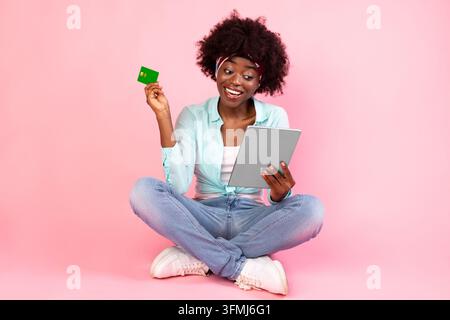Online-Shopping. Glückliche Afroamerikanische Frau Mit Kreditkarte Mit Digitalem Tablet, Die Zahlung Auf Dem Boden Über Rosa Studio-Hintergrund Macht. E-com Stockfoto