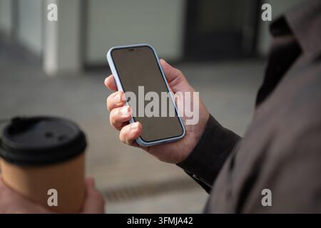 Smartphone in der Hand mit Kaffee im Freien Stockfoto